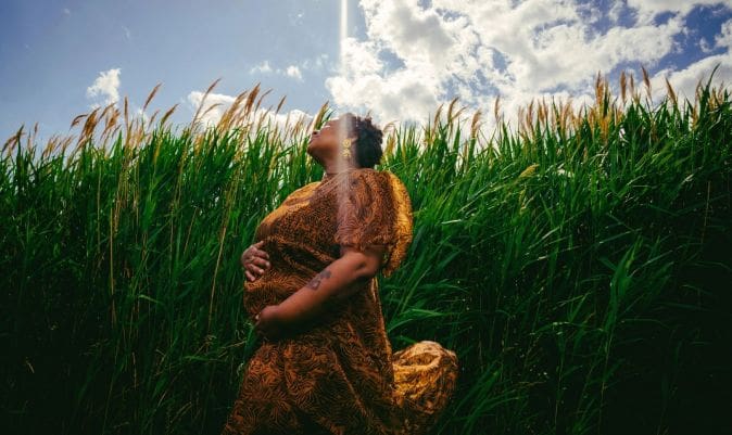 A woman standing in tall grass with her arms crossed.