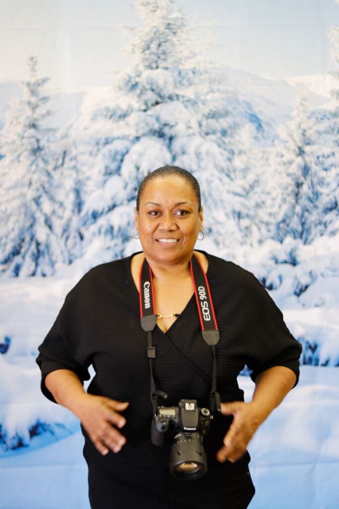 A woman holding a camera in front of snow covered trees.